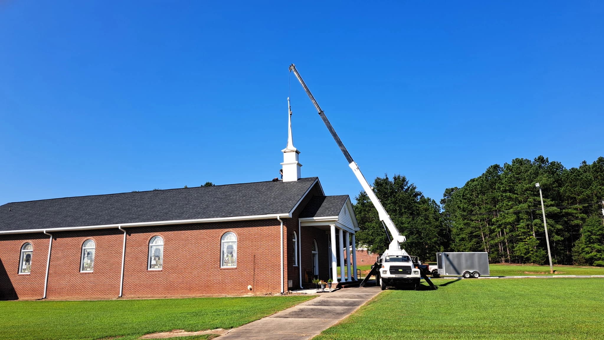 Boom truck crane lifting and positioning a white church steeple onto a brick church roof