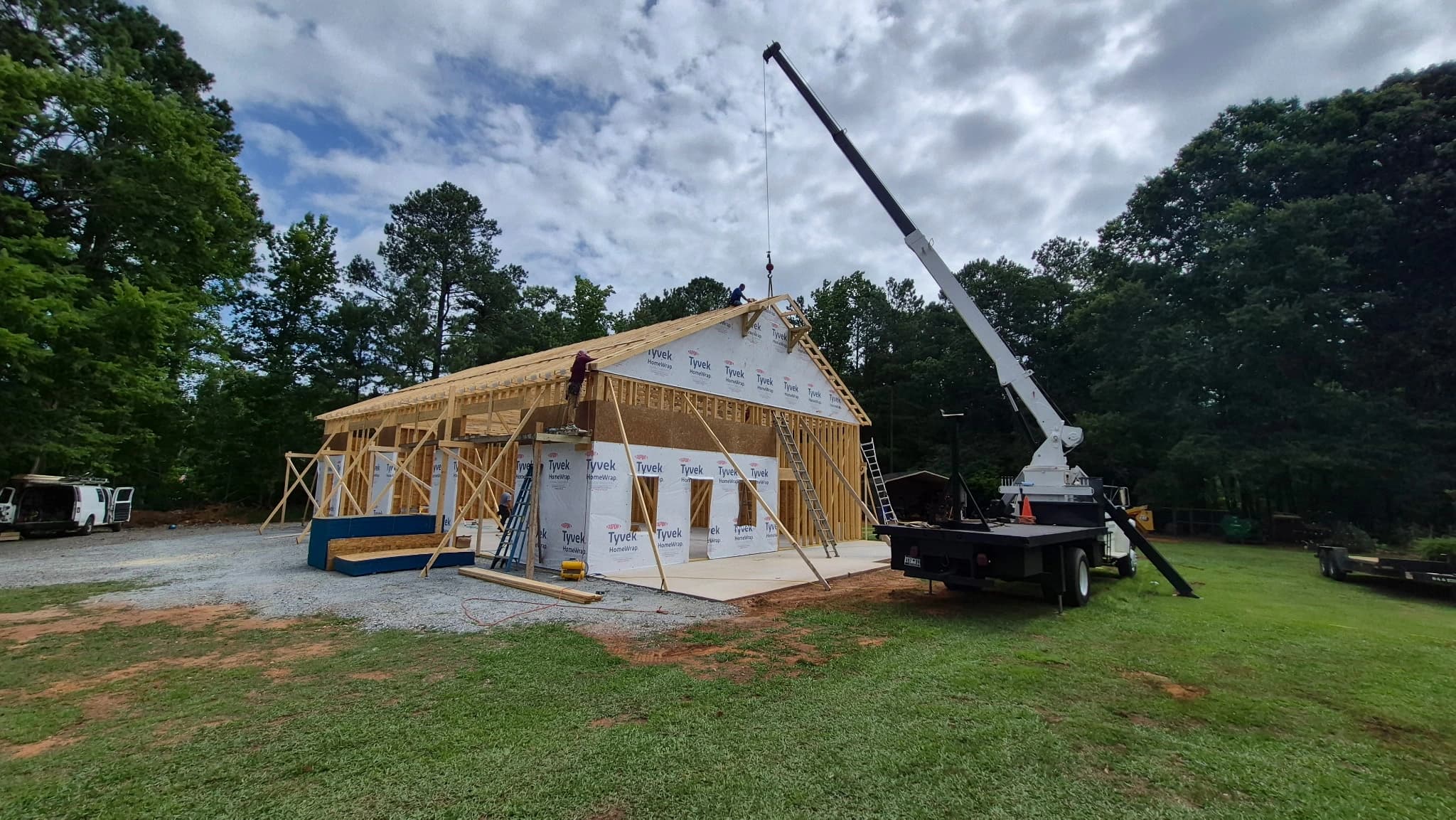 Boom truck crane lifting and setting wood roof trusses on a framed building